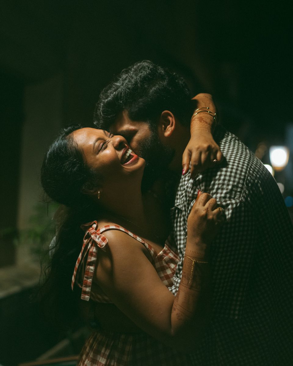 Steeja and Arjun laughing in a close embrace, lit warmly against the dark.
