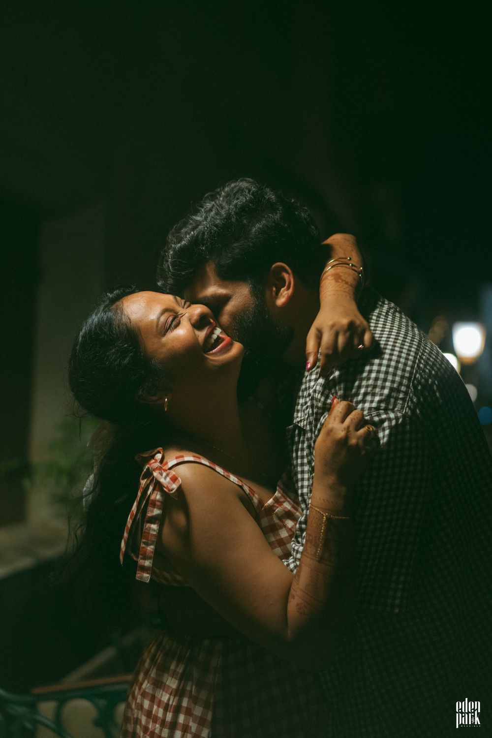 Steeja laughing with her head tipped back as Arjun leans in close, lit warmly against the dark.
