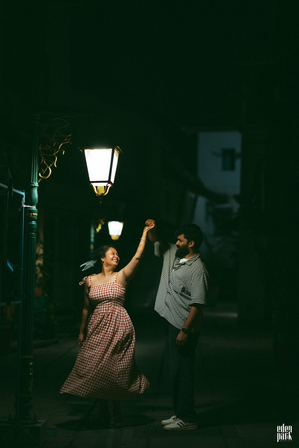 On a lamplit street after dark, Steeja lifts her arm and turns towards Arjun, who holds her hand as she spins.